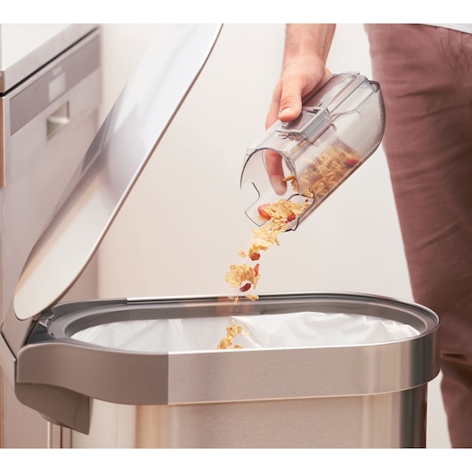BLACKDECKER BHFEA18D1 vacuum dustbin being emptied into a kitchen trash can, close-up photography.