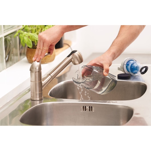 Photo of BLACKDECKER BHFEA420J dust container being rinsed under kitchen faucet near a stainless steel sink.