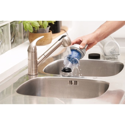 BLACKDECKER BHFEA420J vacuum filter being rinsed under a kitchen faucet above a stainless steel sink.