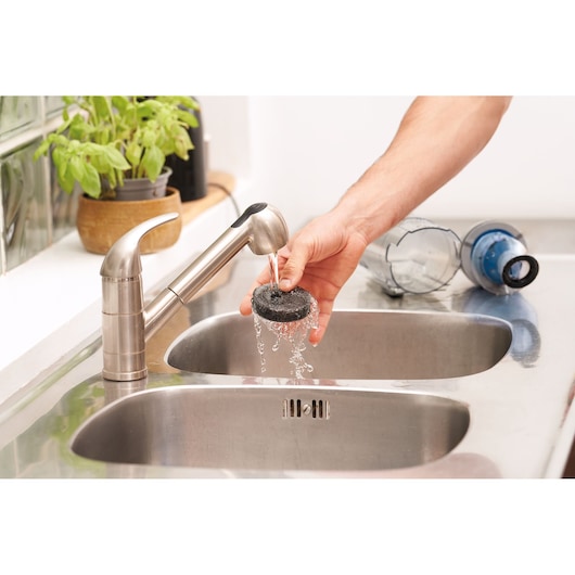 BLACKDECKER BHFEA420J filter being rinsed under faucet in kitchen sink, vacuum dust container nearby.