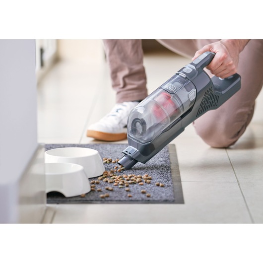 BLACKDECKER BHFEA520J handheld vacuum cleaning pet food near white bowls on gray mat.