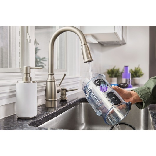 BLACKDECKER BHFEA640WP vacuum dustbin being rinsed under kitchen faucet, countertop and soap dispenser visible.