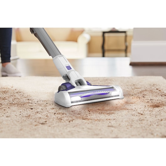 BLACKDECKER BHFEV1825CP cordless vacuum cleaner cleaning a dirty carpet in a living room.