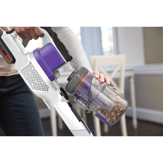 BLACKDECKER BHFEV1825CP cordless vacuum in white and purple, shown emptying dust container indoors.