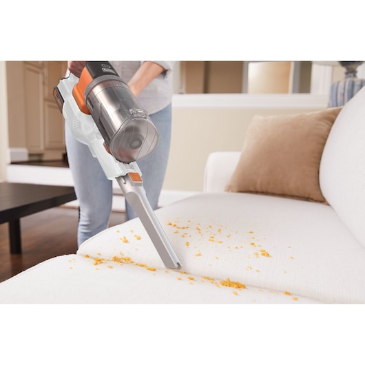 BLACKDECKER BHFEV1825C cordless vacuum cleaning crumbs from a white sofa in a living room.