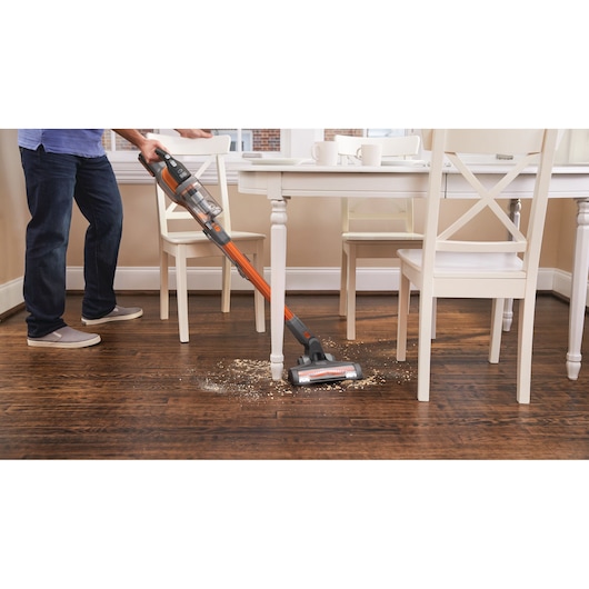 BLACK+DECKER BHFEV182C2 cordless stick vacuum cleaning debris from hardwood floor near dining table.