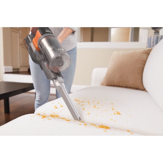 Photo of BLACKDECKER BHFEV182C2 handheld vacuum cleaning crumbs from a white sofa in a living room.