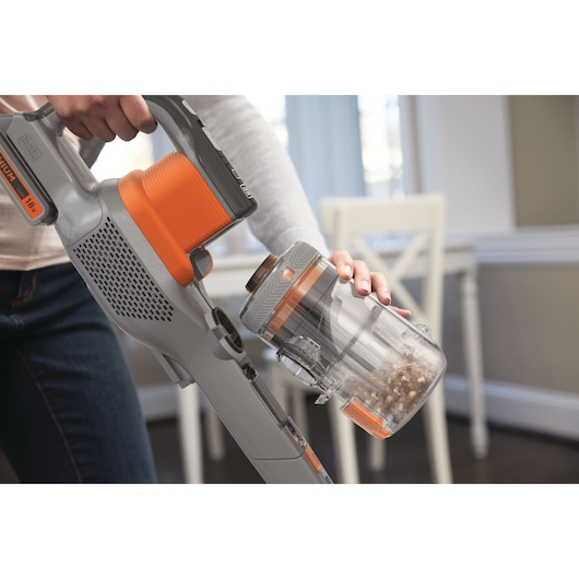 BLACKDECKER BHFEV182C cordless vacuum cleaner with orange accents, showing dust container being emptied.