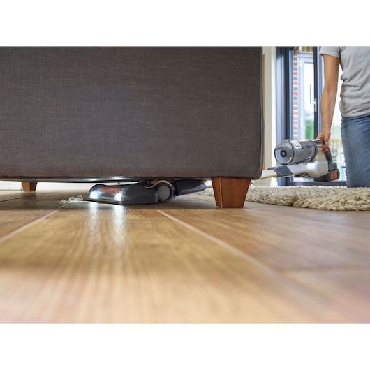 BLACKDECKER BHFEV36B2DW cordless vacuum cleaner cleaning under sofa on wooden floor, handheld view.