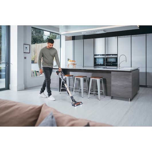 BLACKDECKER BHFEV36B2DW cordless stick vacuum in use on light kitchen floor near island stools.