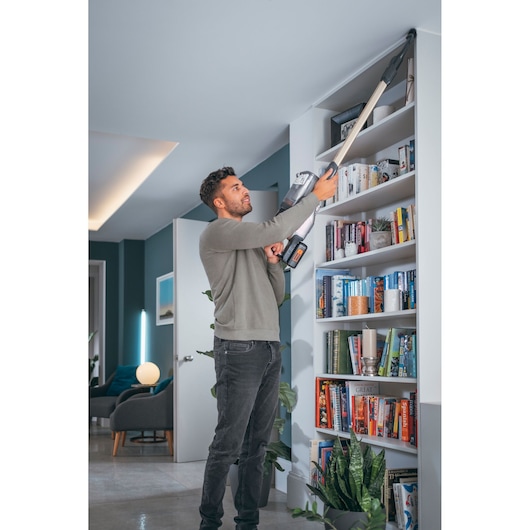 BLACKDECKER BHFEV36B2DW cordless vacuum cleaning top of bookshelf in modern living room.