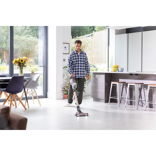 BLACKDECKER BHFEV36B2DW stick vacuum in use on light kitchen floor, modern home interior, side angle.