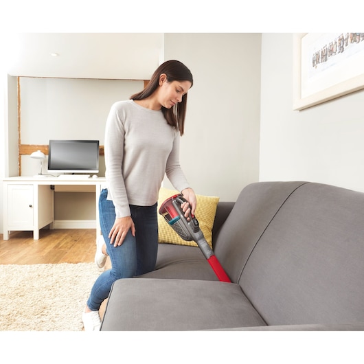BLACKDECKER BHHV315J handheld vacuum cleaner cleaning gray sofa in living room setting.