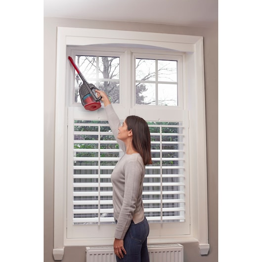 BLACKDECKER BHHV315J handheld vacuum cleaning window frame with long nozzle in home setting.