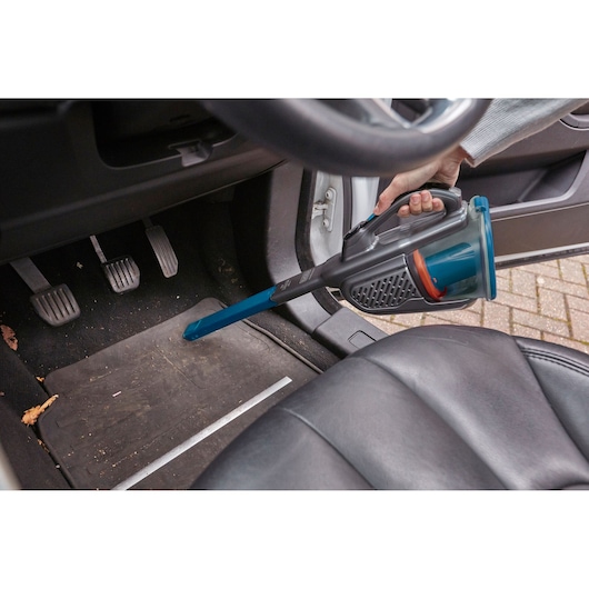 BLACK+DECKER BHHV320B handheld vacuum with extension nozzle cleaning car floor mat near pedals.