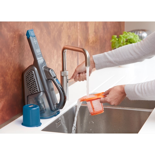 BLACKDECKER BHHV320B handheld vacuum being cleaned, filter rinsed under faucet in kitchen sink, side view.