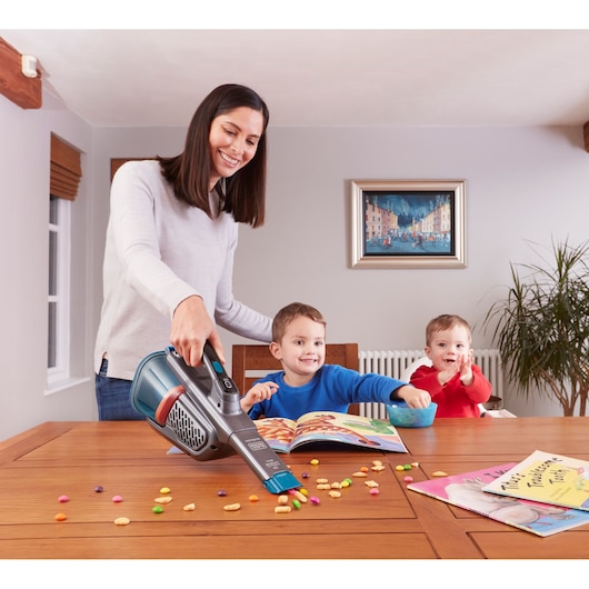 Photo of BLACKDECKER BHHV320J handheld vacuum cleaning crumbs from a wooden table near children in a dining room.