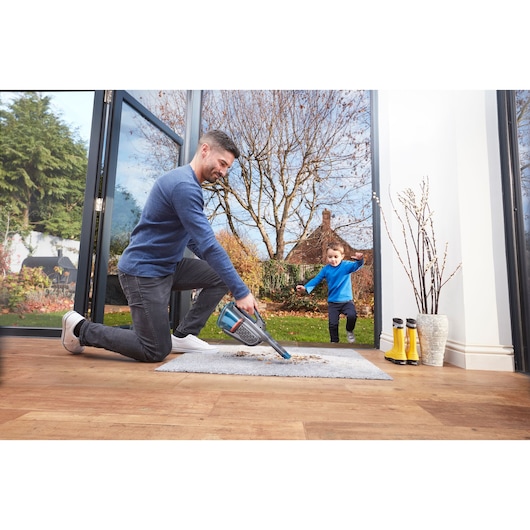 BLACKDECKER BHHV320J handheld vacuum cleaning debris from a rug in a bright indoor setting.