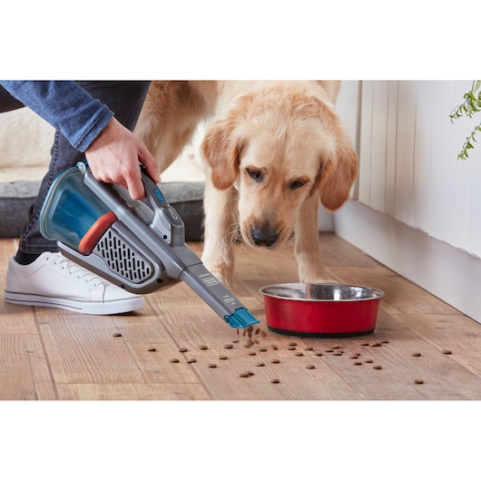 BLACKDECKER BHHV320J handheld vacuum cleaning pet food near red bowl on wooden floor, side angle.