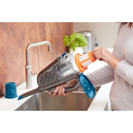 Photo of BLACKDECKER BHHV320J handheld vacuum being cleaned, showing filter removal over a kitchen sink.