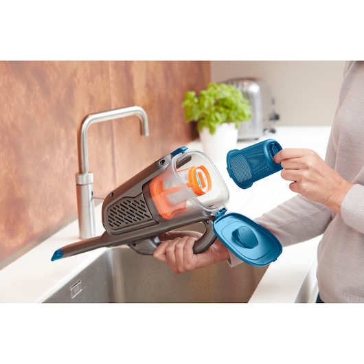 BLACKDECKER BHHV320J handheld vacuum cleaner with dust container open for cleaning over a kitchen sink.