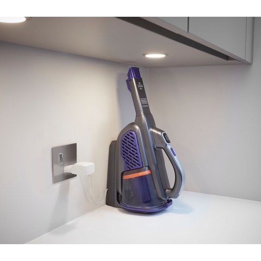 BLACKDECKER BHHV520BFP handheld vacuum in purple and grey, charging on a countertop under a cabinet.
