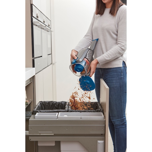 BLACK+DECKER BHHV520BF handheld vacuum being emptied into kitchen trash bin, showing open dust container.