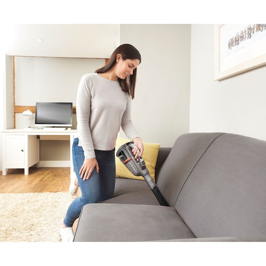 BLACKDECKER BHHV520JF handheld vacuum cleaning sofa in modern living room.