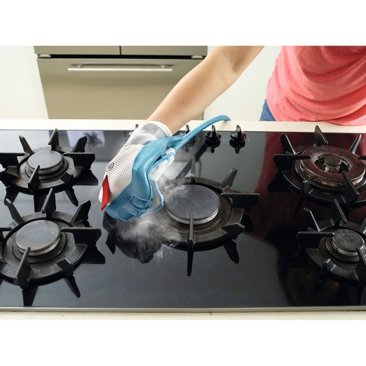 BLACKDECKER BHSM1615DSM steam cleaning glove being used to clean a black gas stove top with visible steam.