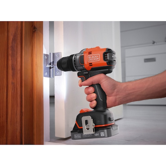 BLACK+DECKER cordless drill BLD682XN used to screw a door hinge, orange and black design, close-up view.