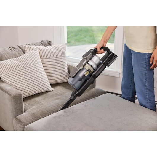 Photo of BLACKDECKER BSV520BL2P cordless vacuum cleaner cleaning a gray sofa with striped pillows.