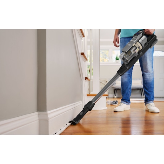 BLACKDECKER BSV520BL2P cordless stick vacuum cleaning baseboard in living room.