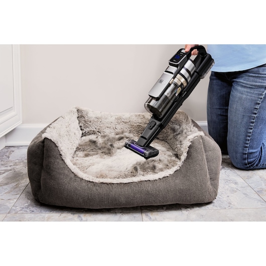 BLACKDECKER BSV520BL2P cordless vacuum cleaning a gray plush pet bed on tile floor, handheld mode.