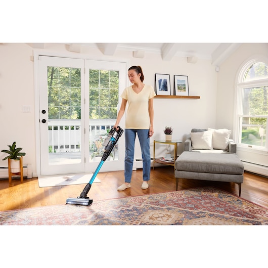 BLACKDECKER BSV520BRB cordless stick vacuum in use on hardwood and rug in bright living room.