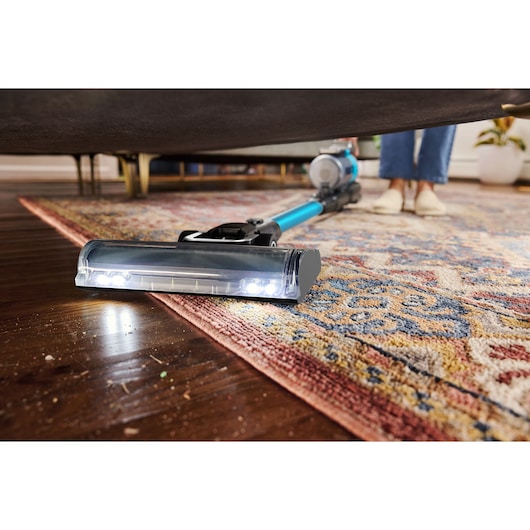 BLACKDECKER BSV520BRB stick vacuum with LED lights cleaning under a sofa on a patterned rug and hardwood floor.