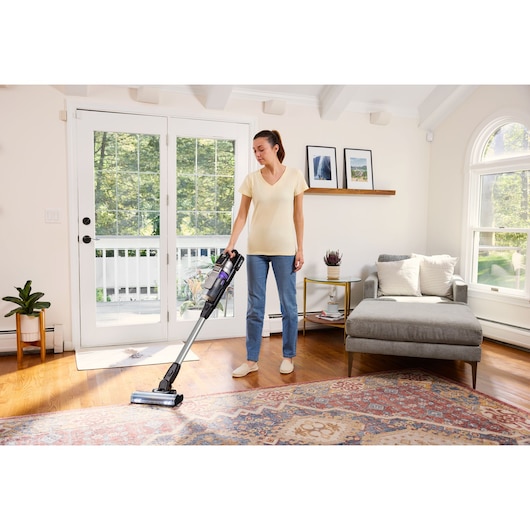 BLACKDECKER BSV520BRP cordless stick vacuum cleaner in use on hardwood and rug in a bright living room.