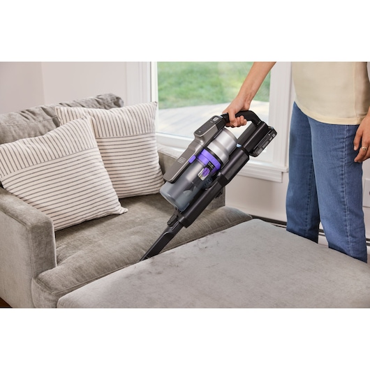 BLACKDECKER BSV520BRP cordless stick vacuum cleaning a gray sofa in a home setting.