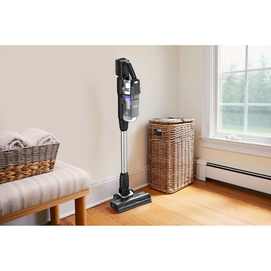 BLACKDECKER BSV520BRP cordless stick vacuum cleaner standing upright on hardwood floor near wicker basket.