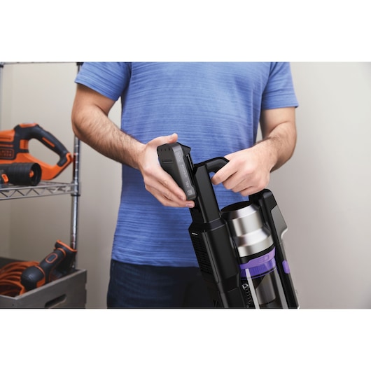 Photo of person inserting battery into BLACK+DECKER BSV520BRP cordless vacuum cleaner, close-up view.