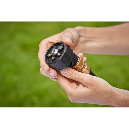 Photo of hands adjusting BLACK+DECKER BZO51N1 garden hose nozzle with black and brass design outdoors.