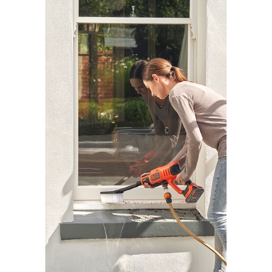 BLACK+DECKER BZOSBSK3 power scrubber with hose attachment cleaning exterior window ledge.
