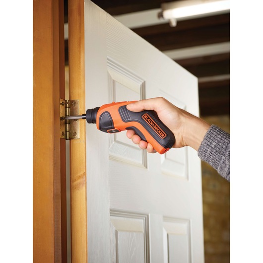BLACK+DECKER CS3651LC orange cordless screwdriver used on a door hinge.