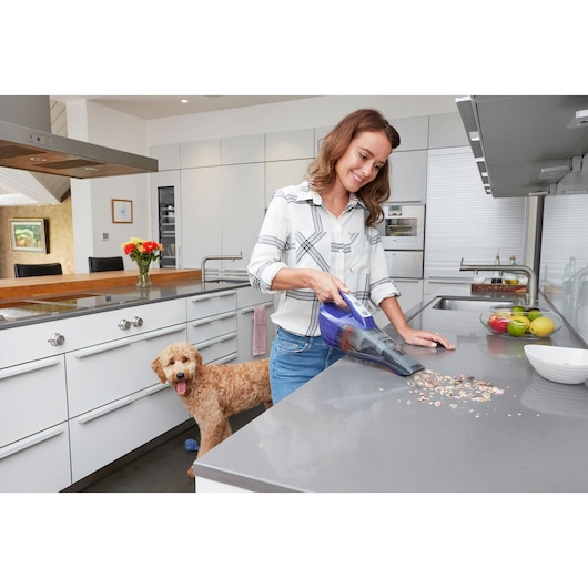 BLACKDECKER DVB315JP handheld vacuum cleaning countertop in modern kitchen, woman holding appliance.
