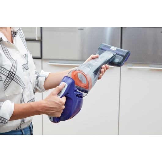 Photo of BLACK+DECKER DVB315JP handheld vacuum cleaner with purple and orange accents, shown in use indoors.