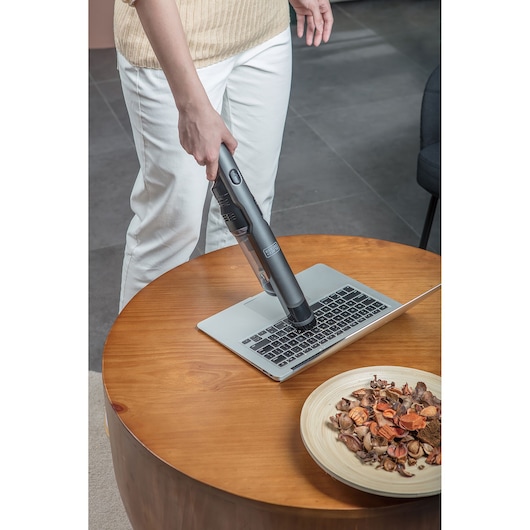 BLACKDECKER DVC320B21 handheld vacuum cleaning laptop keyboard on wooden table, side angle