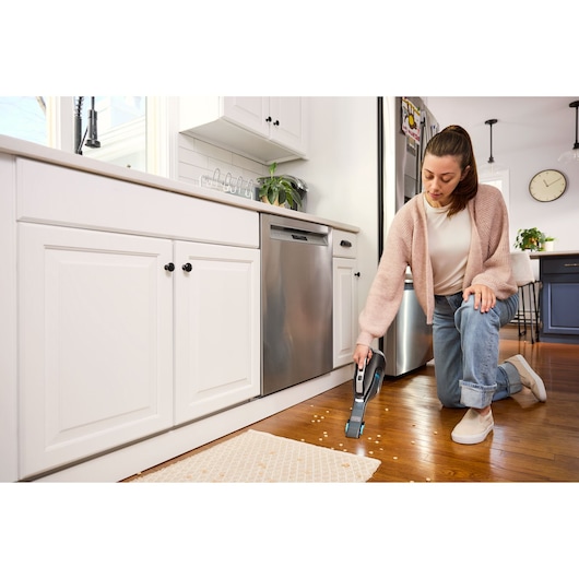 BLACKDECKER DVD320B handheld vacuum cleaning crumbs on hardwood kitchen floor.