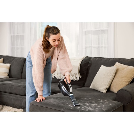 BLACKDECKER DVD320J handheld vacuum cleaning pet hair from a dark sofa in a living room.