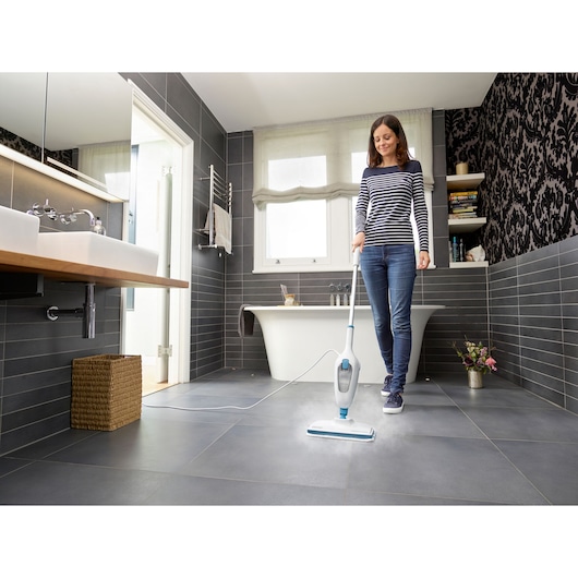 BLACKDECKER FSM13E1 steam mop cleaning dark tile bathroom floor, person using product near bathtub.