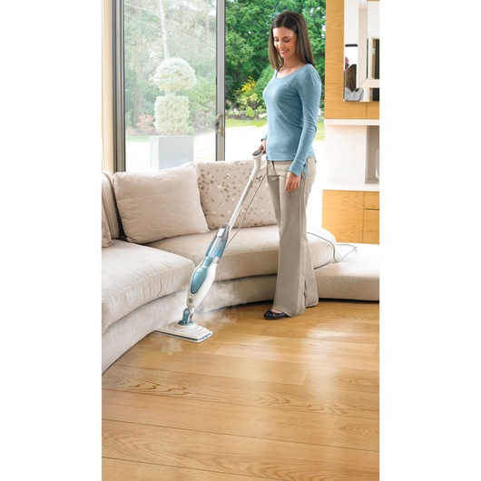 BLACKDECKER FSM16CD steam mop cleaning wooden floor in living room near beige sofa.