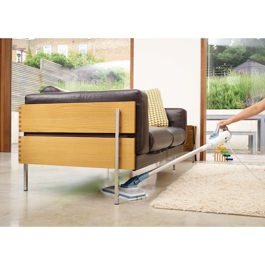BLACKDECKER FSMH1300FX steam mop cleaning under brown sofa on concrete floor, living room angle.